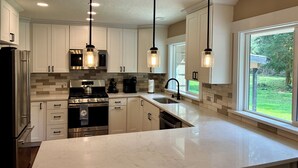Una cocina moderna con armarios blancos, electrodomésticos de acero inoxidable e iluminación colgante.