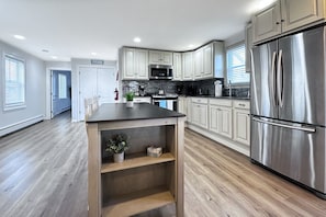 Una cocina moderna con armarios blancos, un refrigerador de acero inoxidable y una isla central con estantes.