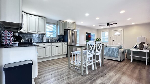 A modern kitchen with white cabinets, a stainless steel refrigerator, and a dining area with a table and chairs. - 1BR Apt | High Speed WiFi | Washer/Dryer | Coffee (Seaside Heights)