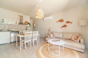 Eine moderne Küche mit weißen Schränken, ein Essbereich mit rundem Tisch und Stühlen, ein beiges Sofa und Fisch-Wandbilder zur Dekoration.