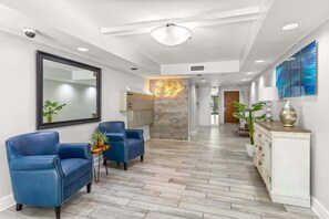 A modern hotel lobby with a reception desk, two blue leather armchairs, a white cabinet, and a large mirror. - Xanadu Retreat - Near Coligny (Hilton Head Island)