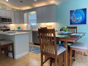 A kitchen with white cabinets, a microwave, a stove, and a dining area with wooden chairs and a table.