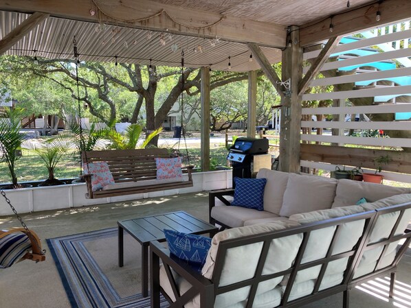 A covered outdoor seating area with a swing, a sofa, and a grill.