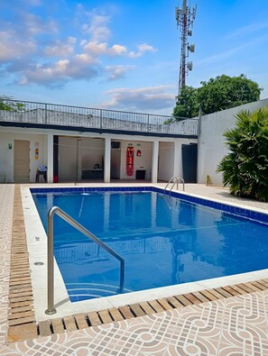 A swimming pool with a metal ladder, surrounded by a tiled deck.