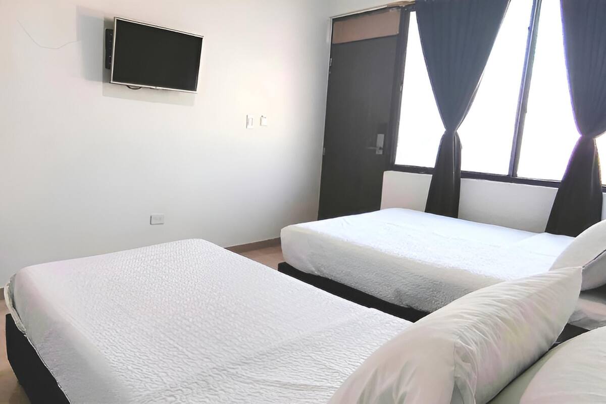A room with two beds, a TV mounted on the wall, and a window with curtains.