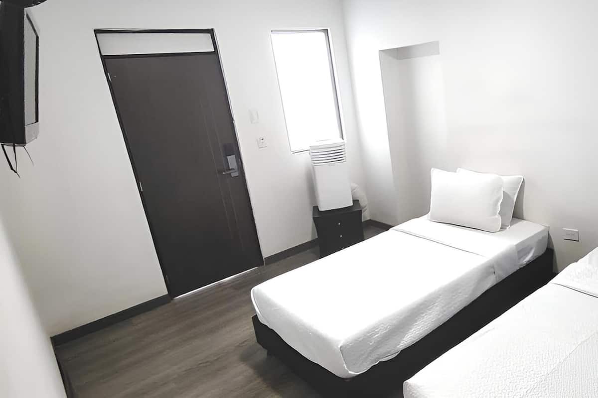 A hotel room with two beds, a door, a window, and a wall-mounted air conditioner.