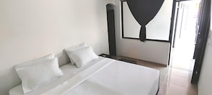 Un dormitorio con cama, almohadas, una ventana con cortina y una puerta.