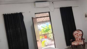 Habitación de hotel con cama, una silla, aire acondicionado y ventilador de techo, con vistas al exterior.