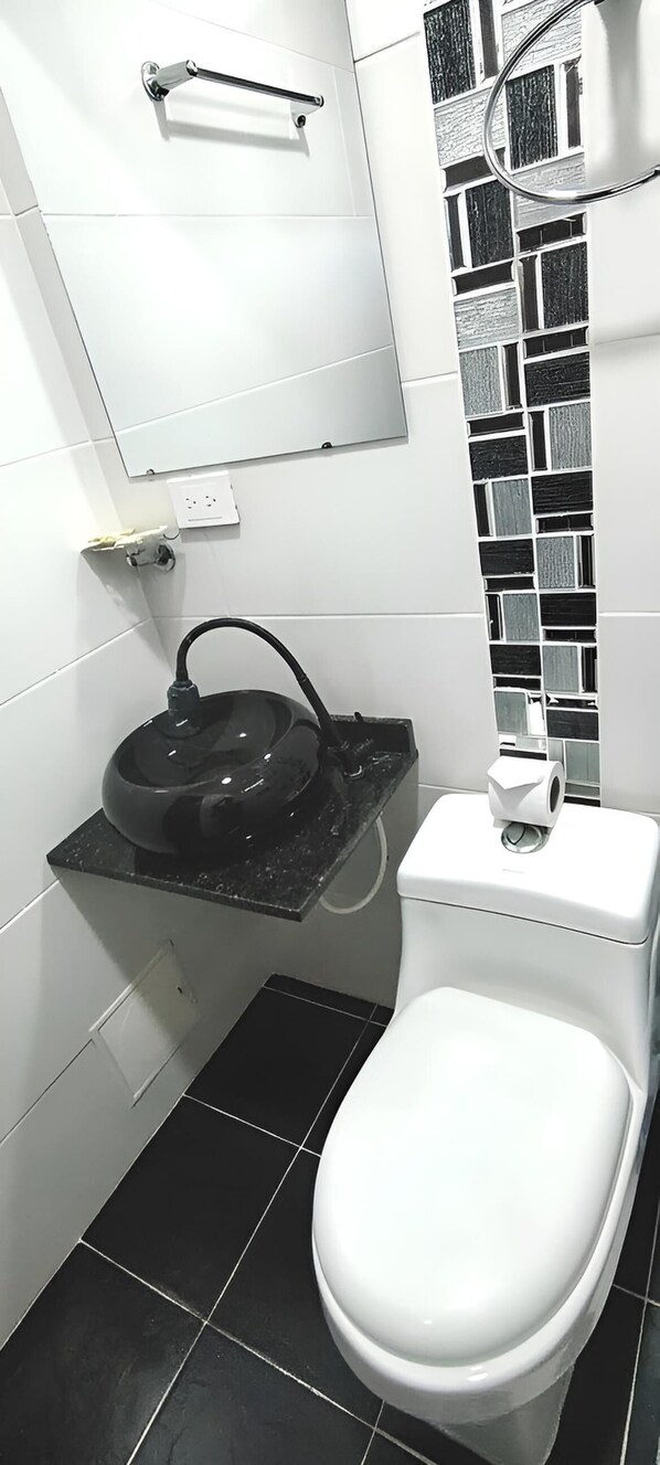 Ein kleines Badezimmer mit Toilette, Waschbecken mit schwarzer Arbeitsplatte, Spiegel und einer schwarz-weißen Küchenrückwand.