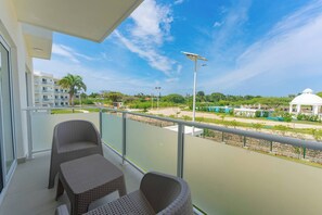 A balcony with wicker chairs, a glass railing, and a view of a resort area including a white dome structure. - Prime Apartment With Fast Internet & Washer in SOV (Sosúa)