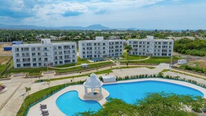 Moderni hotellikompleksi, jossa on useita valkoisia rakennuksia, suuri uima-allas ja huvimaja.