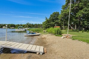 Une jetée au bord du lac avec un bateau, une plateforme en bois et une zone herbeuse avec des arbres.