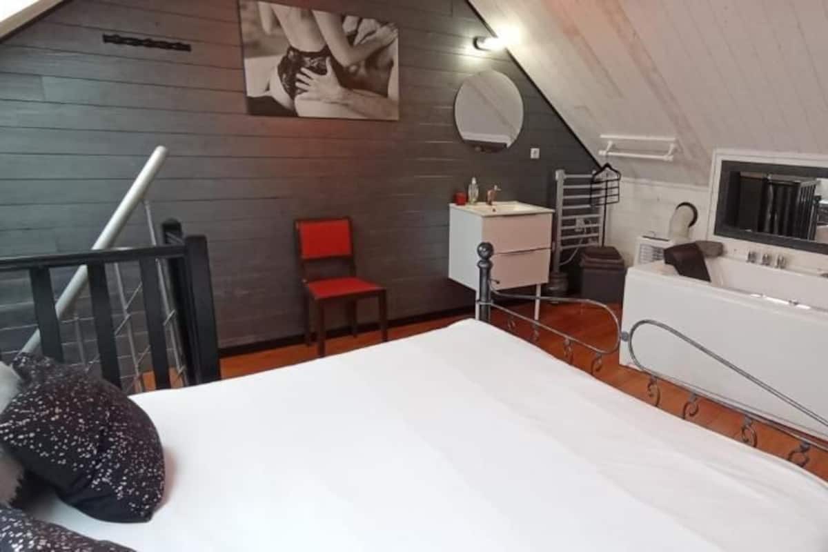 Une chambre à coucher avec un lit, un petit bureau, une chaise, une fenêtre donnant sur un beau paysage et un miroir.