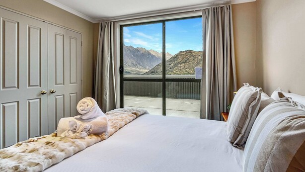 A hotel room with a large bed, a view of mountains, and a sliding door to the balcony.