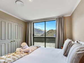 A hotel room with a large bed, a view of mountains, and a sliding door to the balcony. - Lakeside Marina Home, Views and Near Airport (Queenstown)