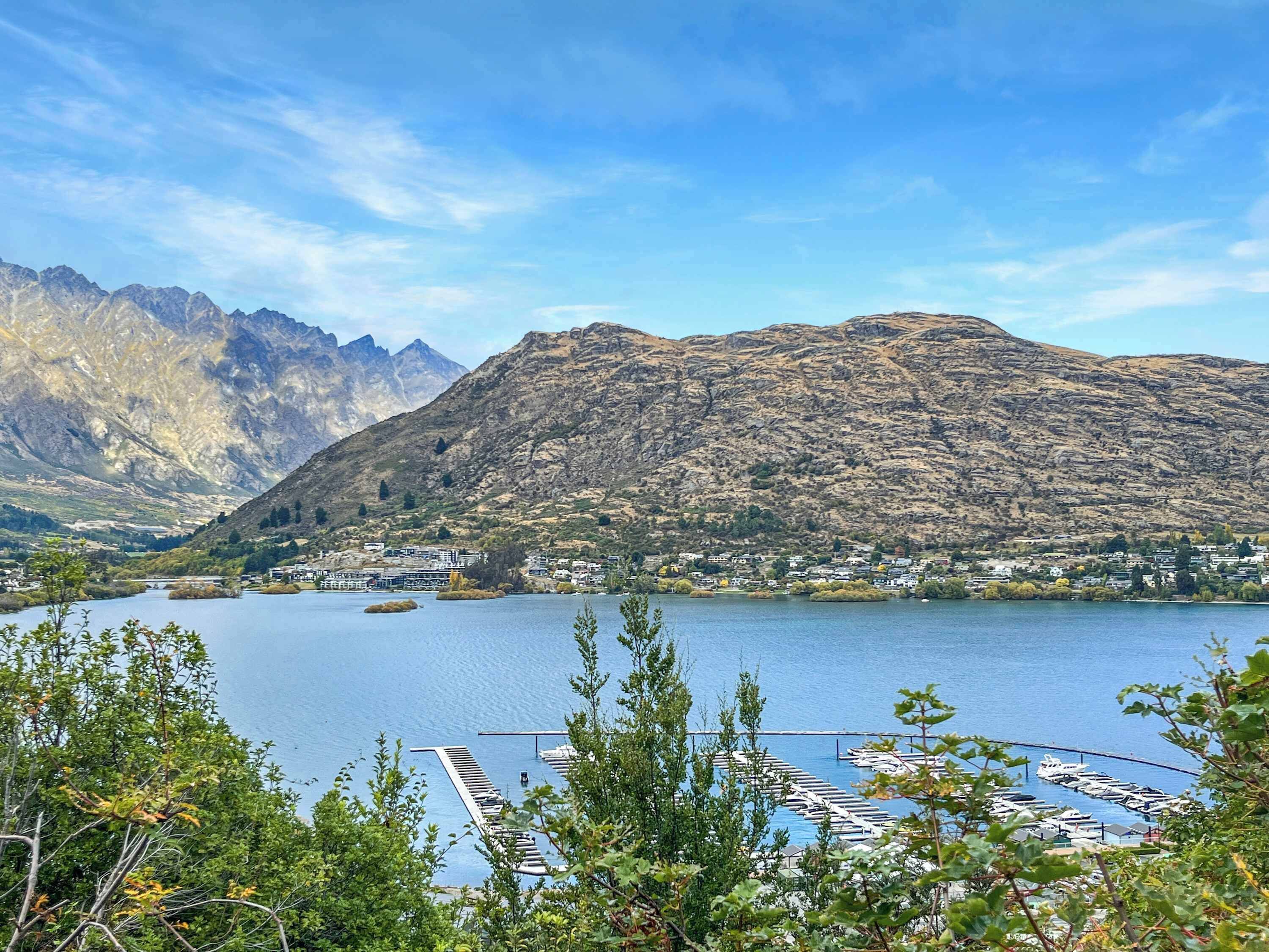 A lake with mountains in the background, a marina with boats, and a town with buildings along the shore.