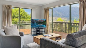 A room with a TV, sofa, and a balcony with a mountain view.