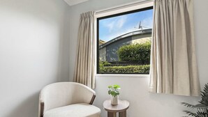 A room with a window, a chair, a small table with a plant, and a potted plant.