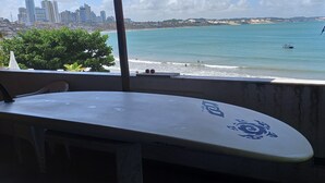 Une planche de surf sur un balcon donnant sur une plage, avec la silhouette d’une ville en arrière-plan.