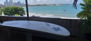 Ein Surfbrett auf einem Balkon mit Blick auf einen Strand und eine Stadtlandschaft im Hintergrund.