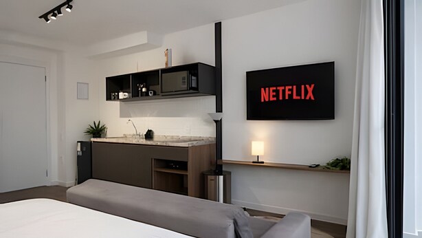 Une chambre d’hôtel moderne équipée d’un lit, d’une kitchenette, d’un téléviseur fixé au mur et d’une lampe de chevet.