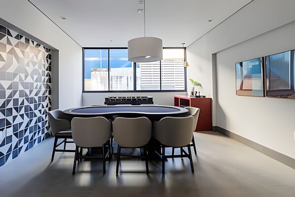 A modern meeting room with a round table, chairs, and a city view through large windows.