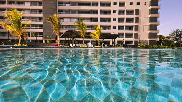 A swimming pool with clear water, surrounded by a building with multiple balconies and palm trees. - Villa Lili, Apartamento lujoso frente al mar, en Santa Marta Colombia (santa marta)