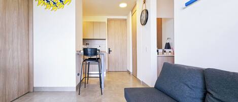 A modern living area with a sofa, a kitchen in the background, and a wall clock.