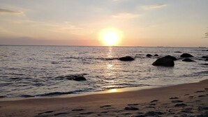 A beach with the sun setting over the ocean, rocks in the water, and footprints on the sand. - Villa Lili, Apartamento lujoso frente al mar, en Santa Marta Colombia (santa marta)