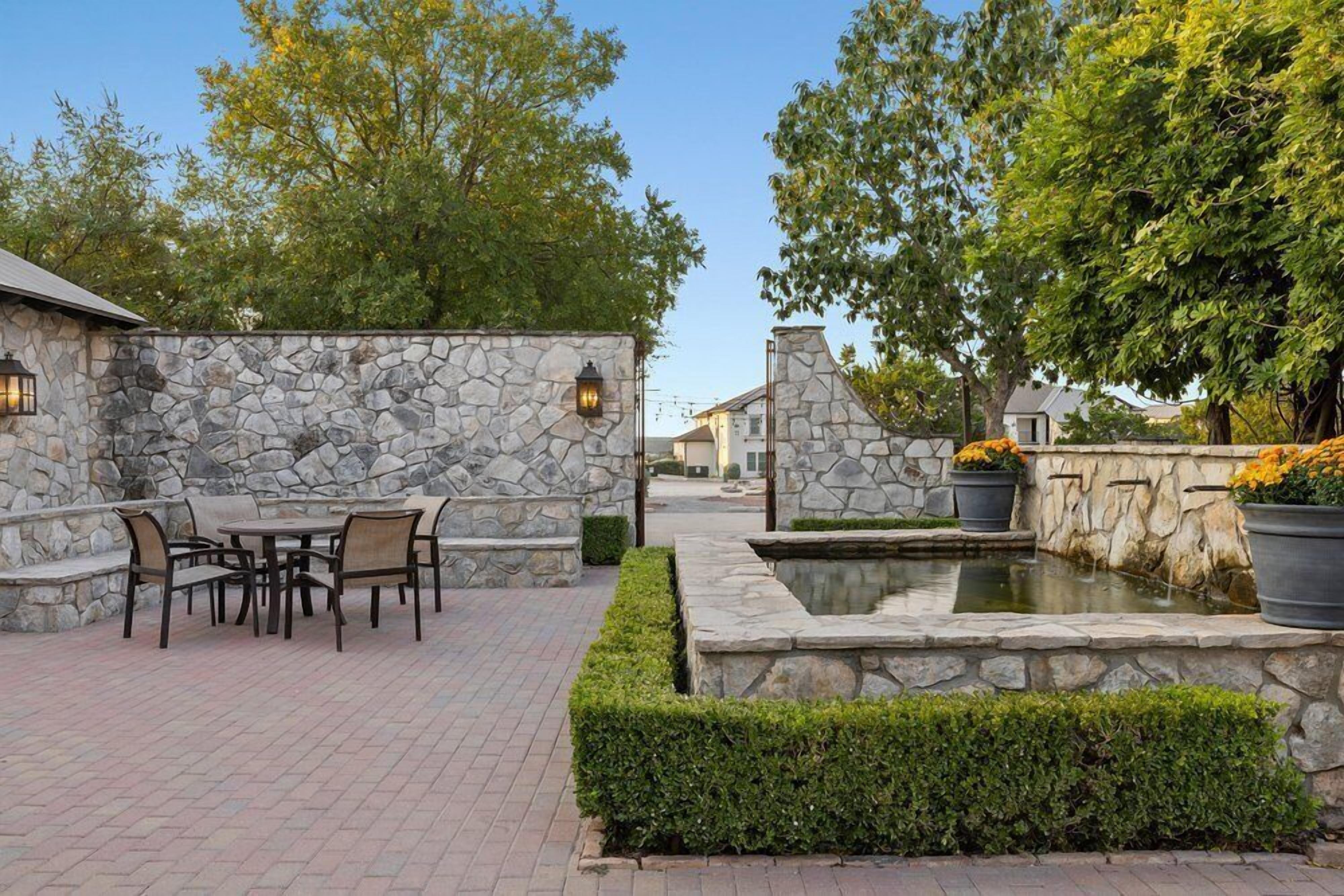 Un patio con paredes de piedra, una mesa con sillas y una pequeña fuente de agua.