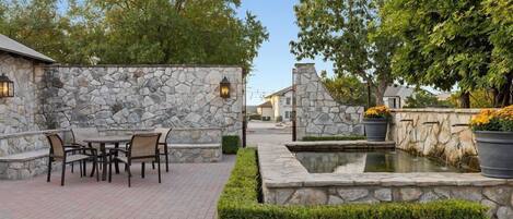 Un patio con paredes de piedra, una mesa con sillas y una pequeña fuente de agua.