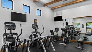 A gym with various cardio machines, a large mirror, and a TV on the wall. - Hill Country | Luxury Nature Retreat | Pool + Trails (Hunt)