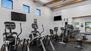 Une salle de sport équipée de divers appareils de cardio, d’un grand miroir et d’un téléviseur fixé au mur.