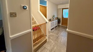 A hallway with a staircase, a thermostat, and a door leading to another room.