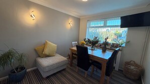 A dining area with a table, chairs, a sofa, a potted plant, and a window with blinds.