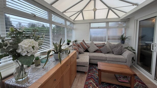 A conservatory with a glass ceiling, a sofa, a wooden coffee table, and a patterned rug.