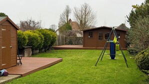 A backyard with a wooden deck, a swing set, and a shed.