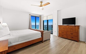 A bedroom with a bed, a dresser, a television, and a balcony with a view. - Fully remodeled ocean front condo with views, pool (Navarre)