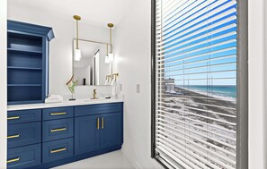 A bathroom with a blue vanity, gold fixtures, and a view of the beach through blinds. - Fully remodeled ocean front condo with views, pool (Navarre)