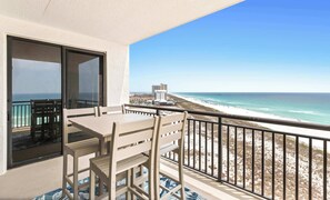 A balcony with a table and chairs, overlooking a beach with a pier and buildings in the distance. - Fully remodeled ocean front condo with views, pool (Navarre)