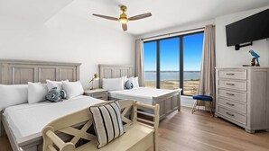 A hotel room with two beds, a desk, a chair, a TV, and a large window with a view of the sea. - Fully remodeled ocean front condo with views, pool (Navarre)