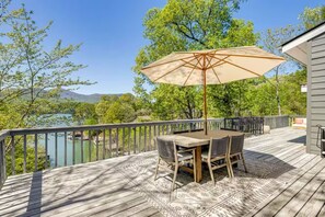 A deck with a table and chairs, a large umbrella, and a view of a lake and trees. - Lake Lure Modern Retreat | Marina Access + Views (Lake Lure)