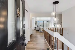 Ein modernes Interieur mit einer Holztreppe, einer schwarzen Tür und Blick in einen Wohnbereich mit Balkon.