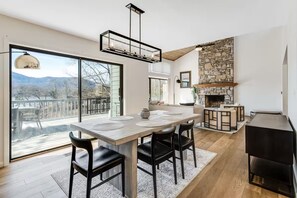 A modern kitchen with a stone fireplace, a dining area with a large table and chairs, and a view through large windows. - Lake Lure Modern Retreat | Marina Access + Views (Lake Lure)