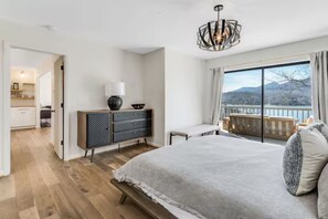 A bedroom with a large bed, a desk, a dresser, and a view of a balcony with a scenic landscape. - Lake Lure Modern Retreat | Marina Access + Views (Lake Lure)
