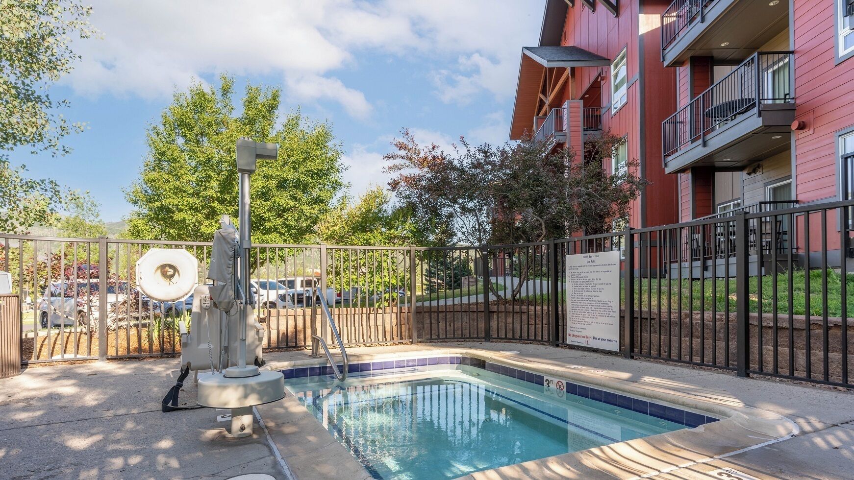 Une piscine entourée d’une clôture en métal, un poste de surveillance pour les sauveteurs et, au fond, un bâtiment doté de balcons.