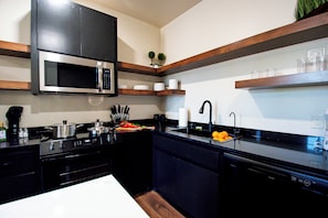 A modern kitchen with a microwave, stove, sink, and wooden shelves. - Brayden Tower Suite #04 with Patio (Lawton)