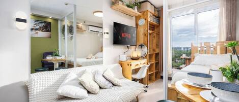 Ein modernes Schlafzimmer mit Bett, Schreibtisch, Fernseher und Blick ins Freie.