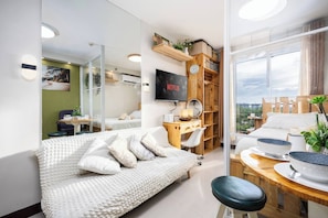 A modern bedroom with a bed, a desk, a TV, and a view of the outdoors. - Cozy Wood-cabin Studio With Balcony & Warm Lighting (Lapu-Lapu)