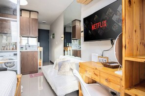 Habitación de hotel moderna con una cama, muebles de madera, un televisor mostrando Netflix, un calendario y un área de lavandería.
